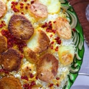 A green platter with rice covered with crispy potatoes.