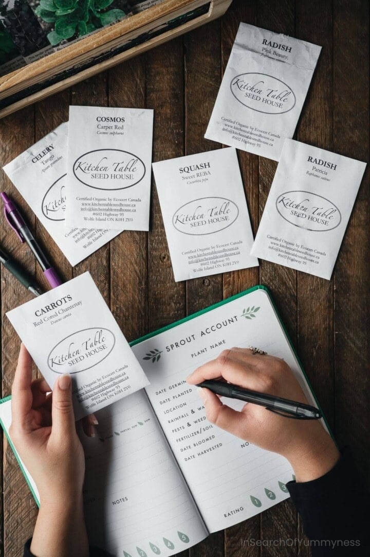 A hand writing in a gardening notebook while another hand holds an envelope of seeds from Kitchen Table Seed House.