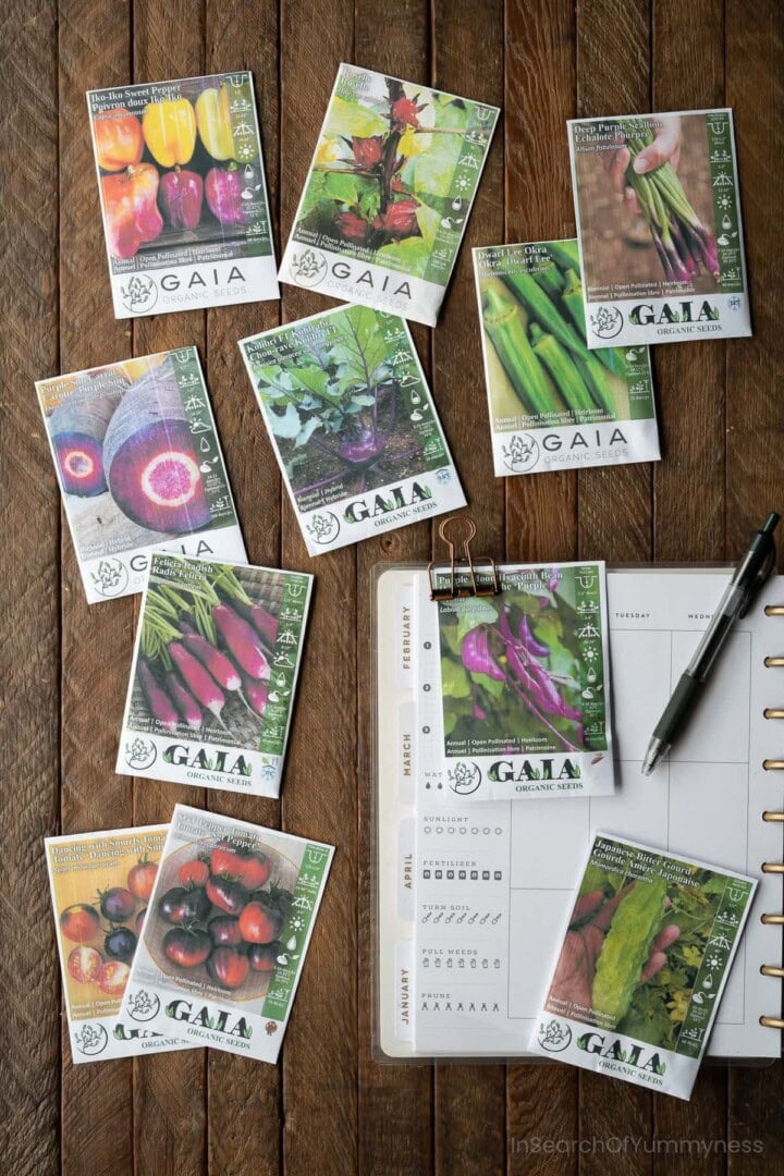 Several vegetable and flower seed packets from Gaia seeds spread out on a table next to a garden planner.