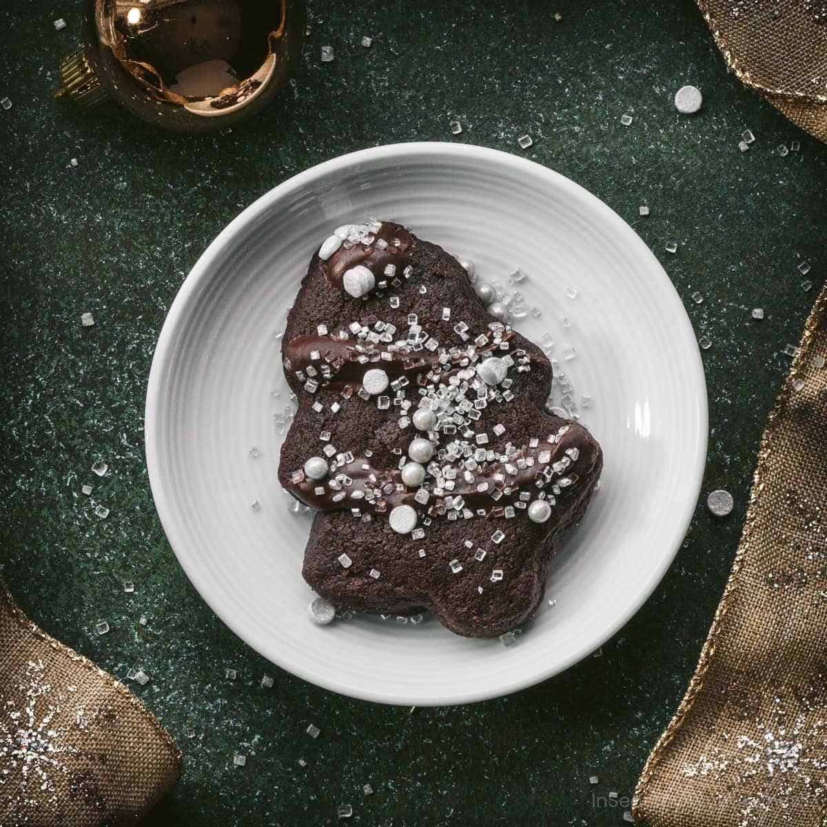 A decorated chocolate shortbread cookie on a small white plate next to Christmas ribbon and decorations.