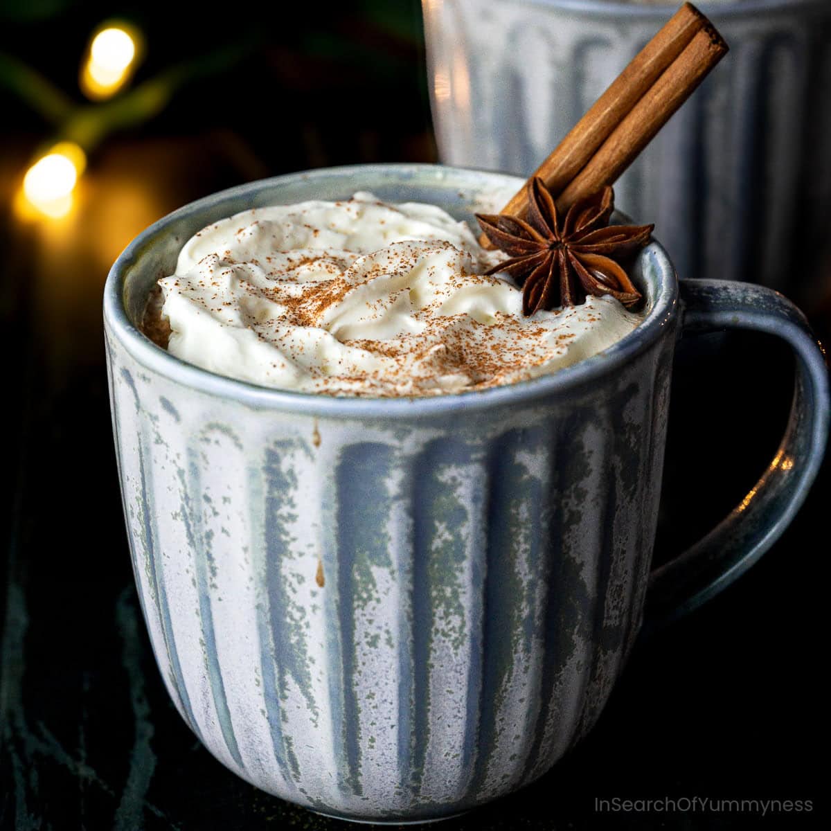 A mug of spiced hot chocolate topped with fresh whipped cream, a star anise pod and a cinnamon stick.