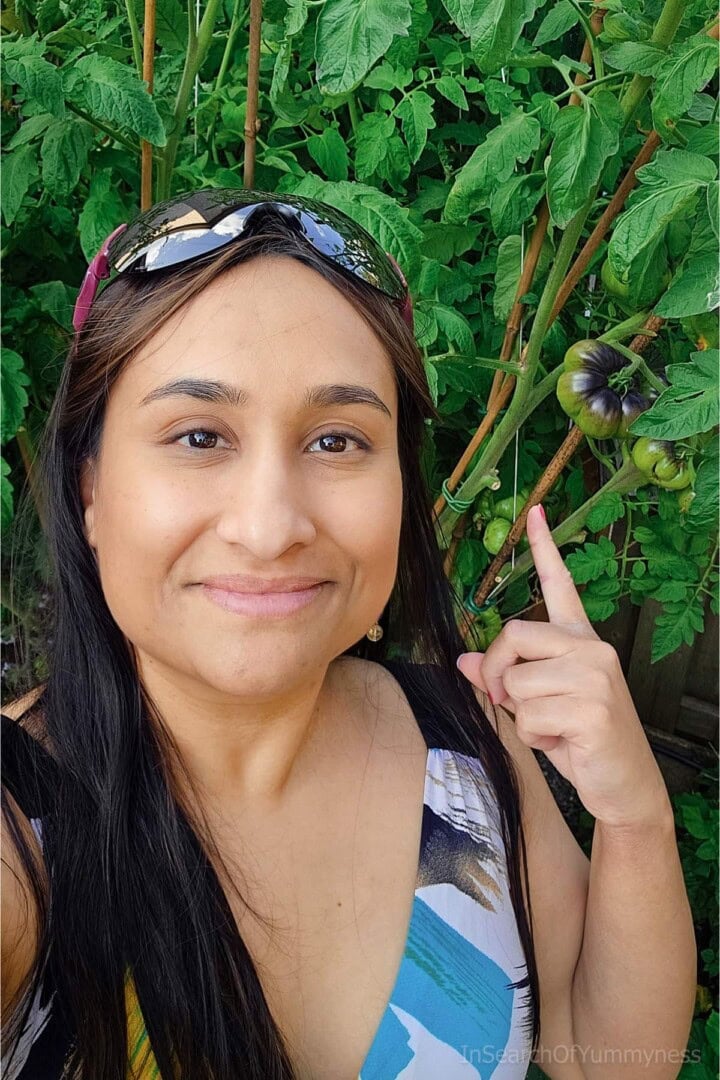 Shareba, editor of In Search Of Yummy-ness, pointing to a tomato that is growing in her garden.