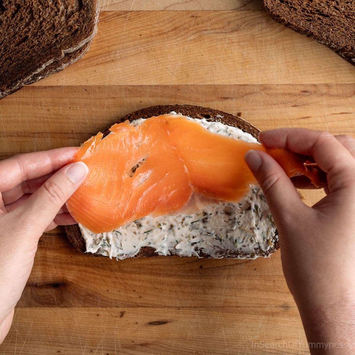 Placing slices of smoked salmon onto a slice of bread spread with lemon dill cream cheese.