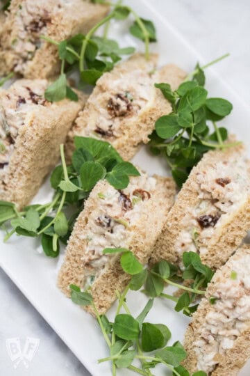 A tray of turkey salad tea sandwiches garnished with fresh oregano.