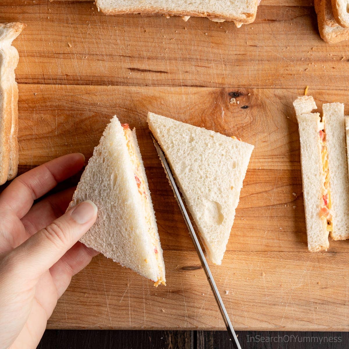 Cutting a pimento cheese tea sandwich into two triangles with a bread knife.