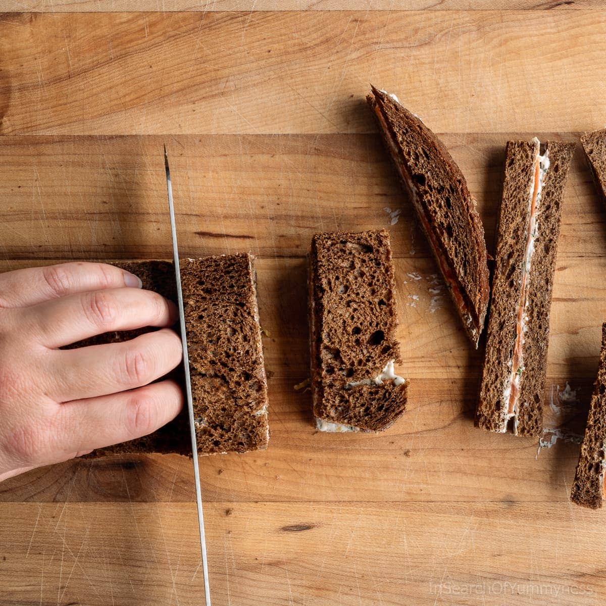 Using a bread knife to cut the smoked salmon sandwich into three tea sandwiches.