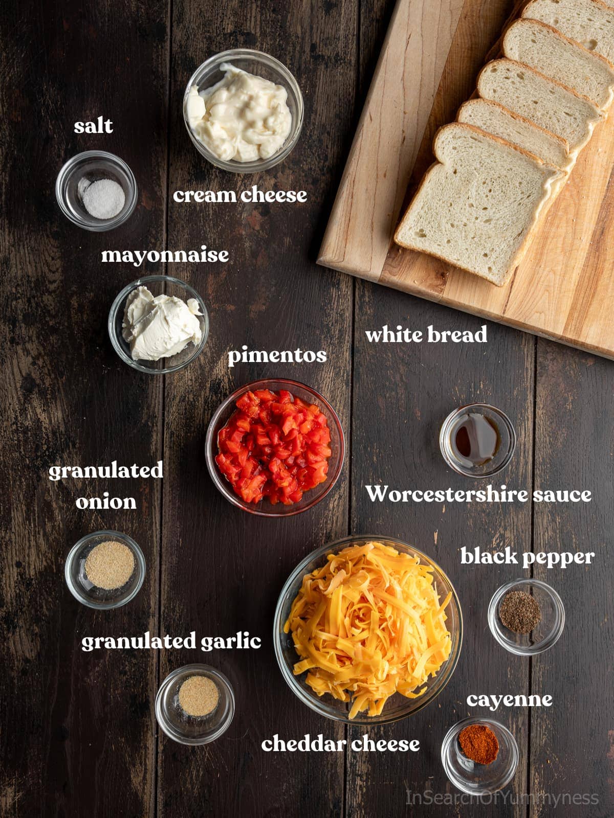 Ingredients to make pimento cheese tea sandwiches in bowls on a table. Ingredients include pimentos, cheddar cheese, mayonnaise, cream cheese, and white bread.
