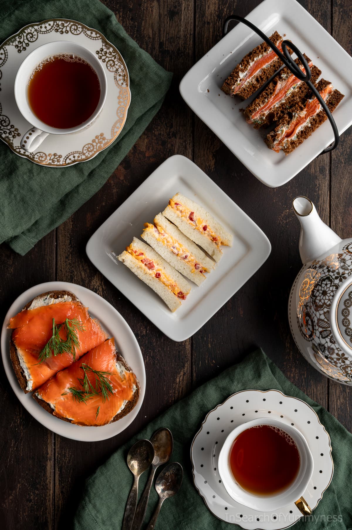 A top-down view of a table set with a teapot, two teacups, and three plates of assorted tea sandwiches.