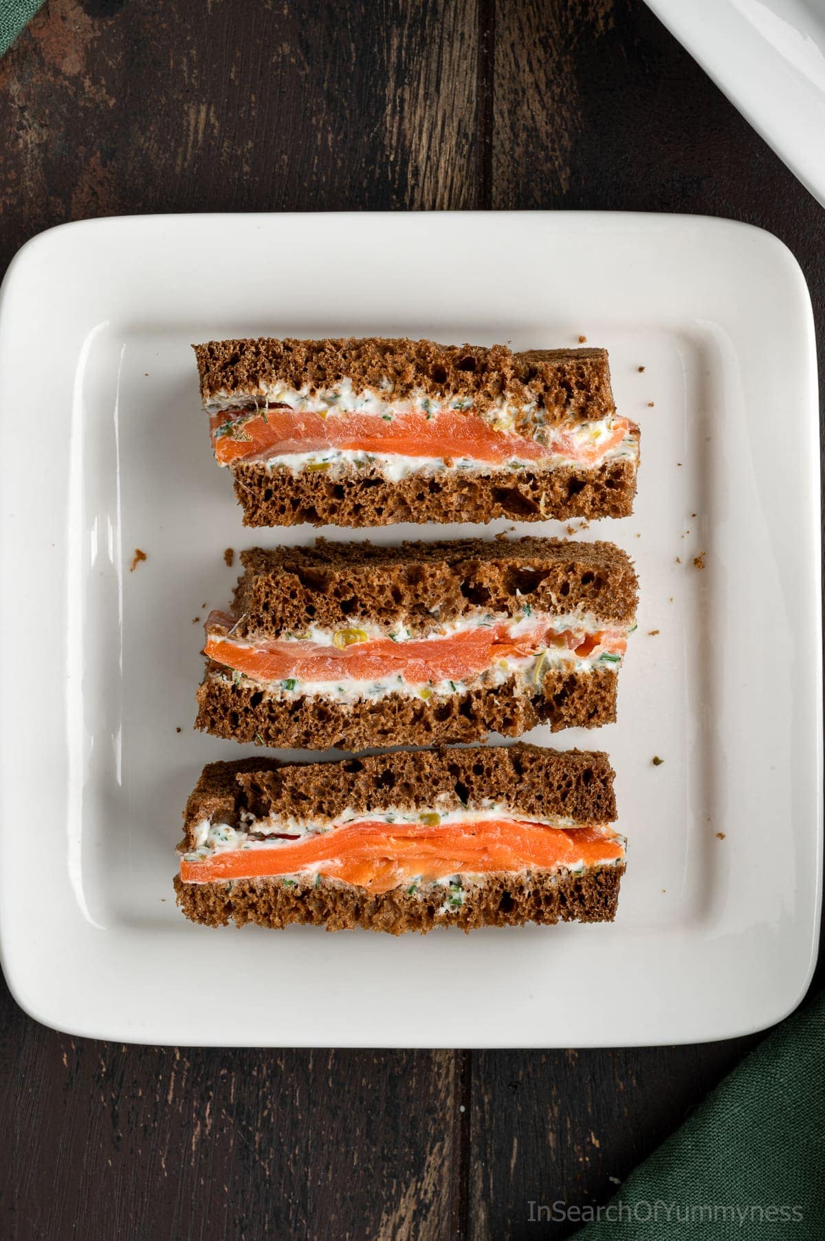 Three smoked salmon tea sandwiches on a square white plate.