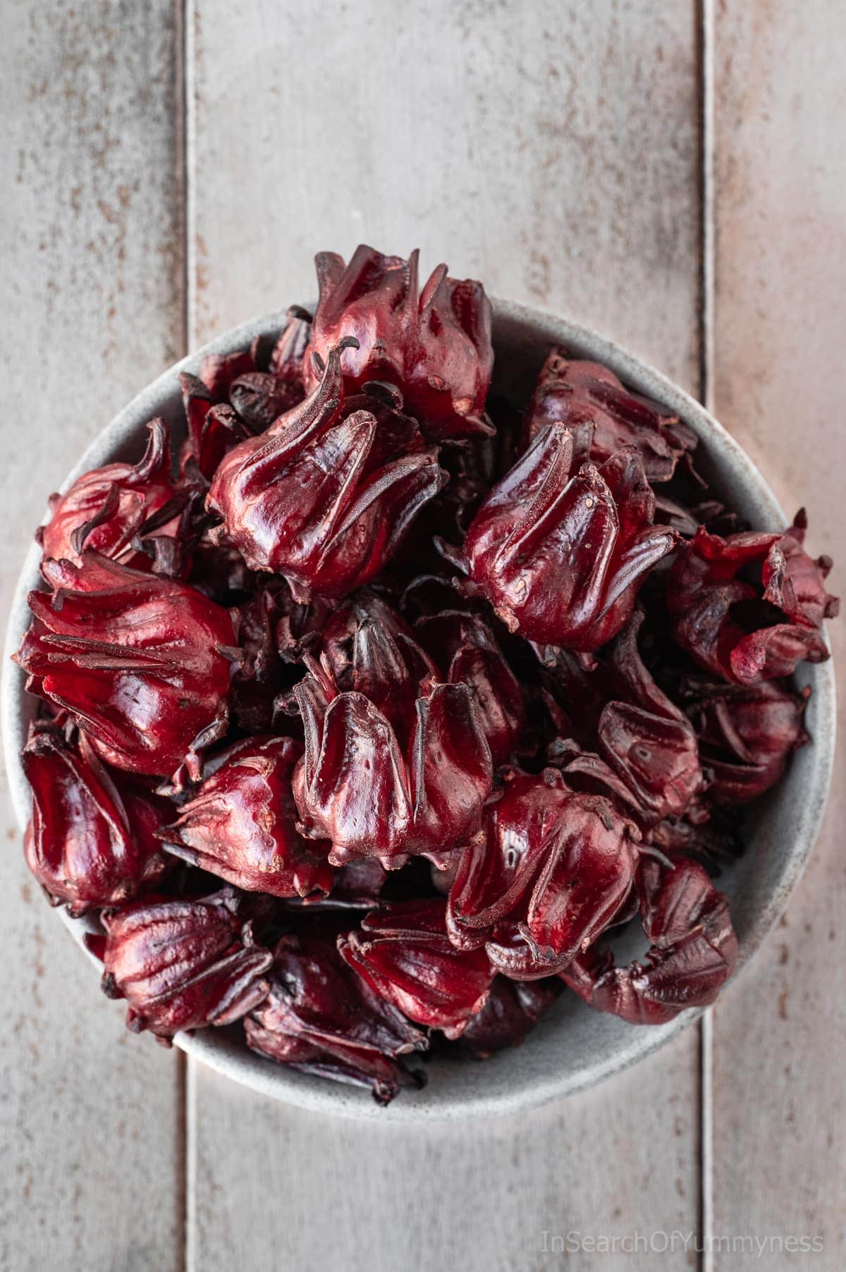 A grey bowl full of ruby-coloured fresh roselle calyxes.