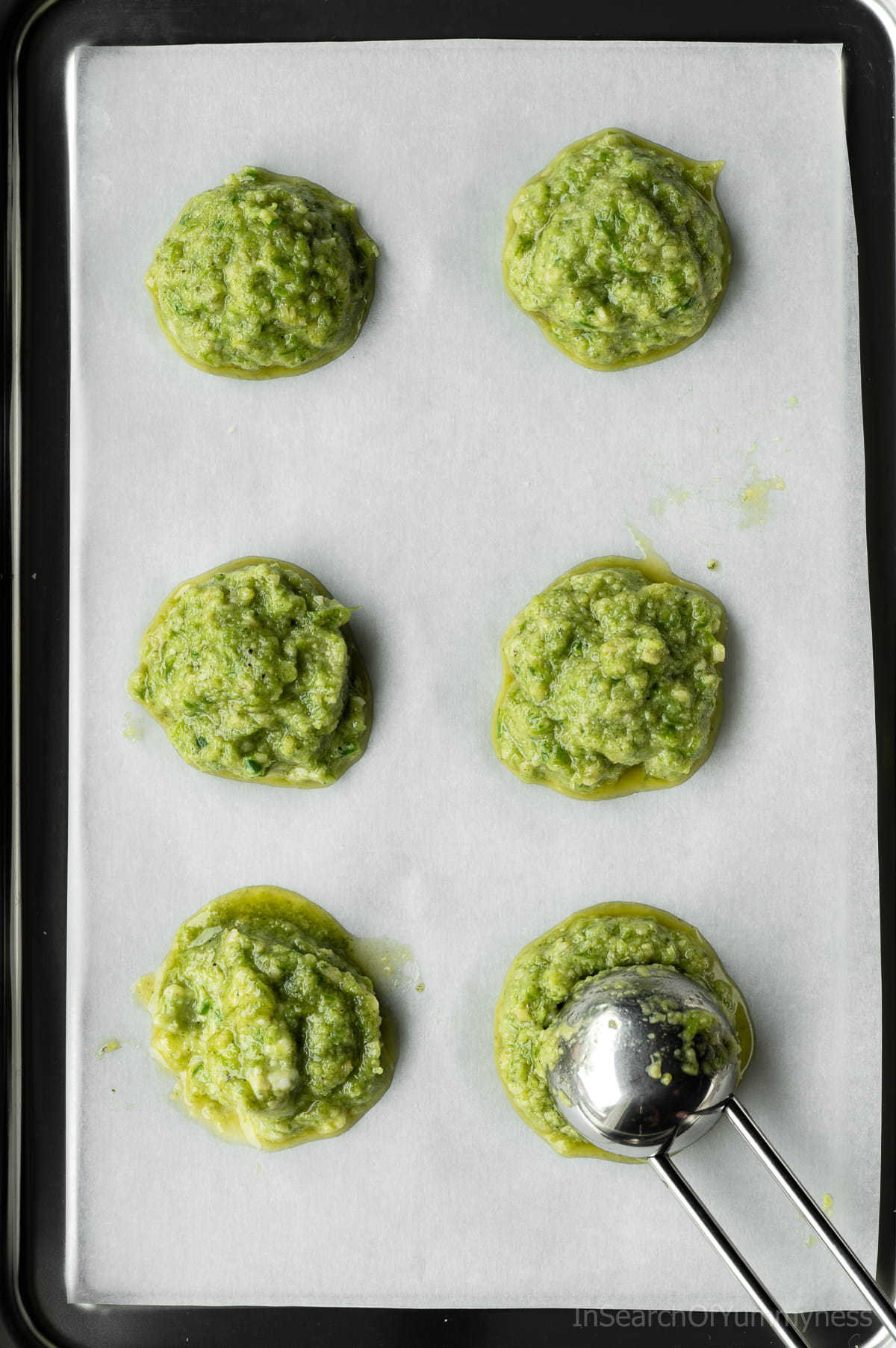 6 tablespoon-sized dollops of garlic scape pesto on a parchment lined baking tray with a tablespoon.
