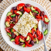 Greek salad with feta cheese in a white bowl with a silver spoon.