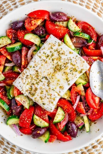 Greek salad with feta cheese in a white bowl with a silver spoon.