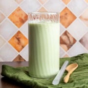 A tall glass of Vietnamese avocado smoothie on a green napkin next to a large straw and a wooden spoon.