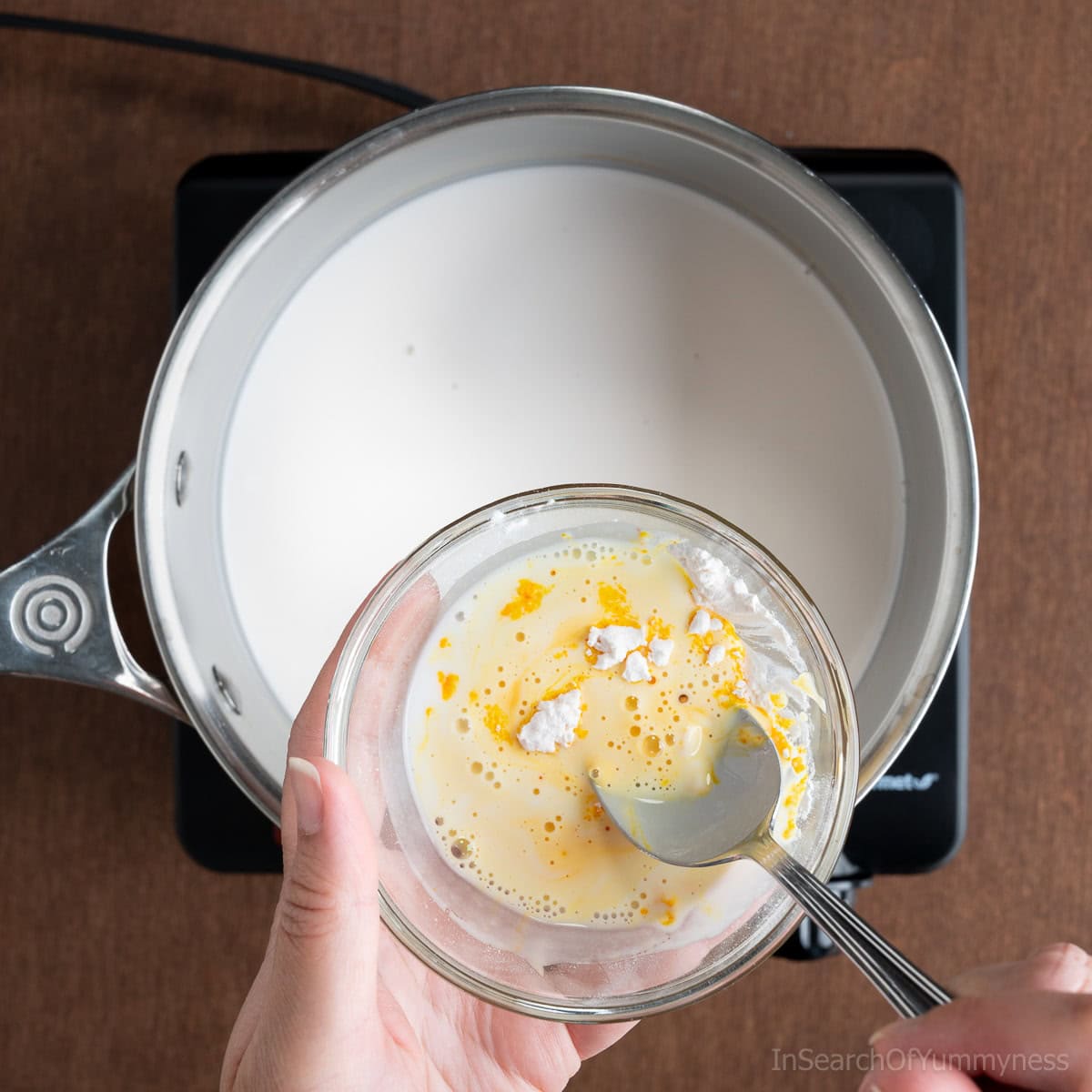 Dissolving custard powder with warm coconut milk in a small glass bowl.