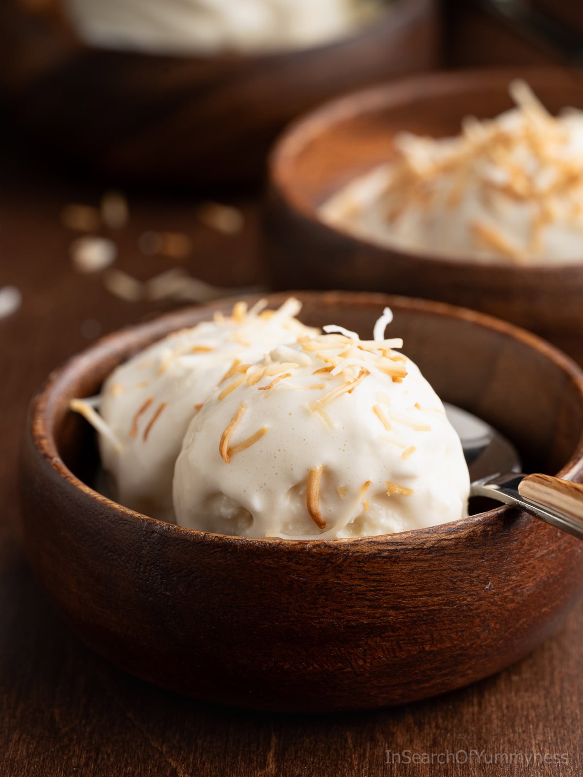 A wooden bowl with two scoops of Trinidad coconut ice cream, topped with toasted coconut.