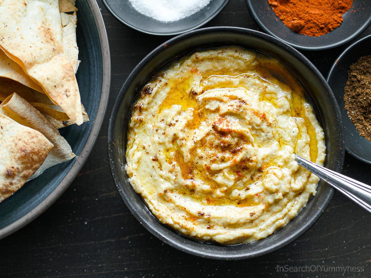 A bowl of creamy hummus drizzled with olive oil and sprinkled with cumin and paprika.