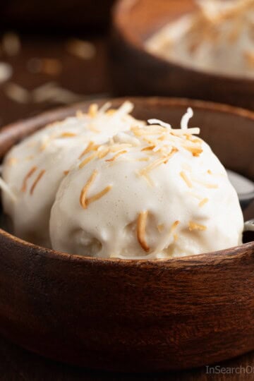 A wooden bowl with two scoops of Trinidad coconut ice cream, topped with toasted coconut.