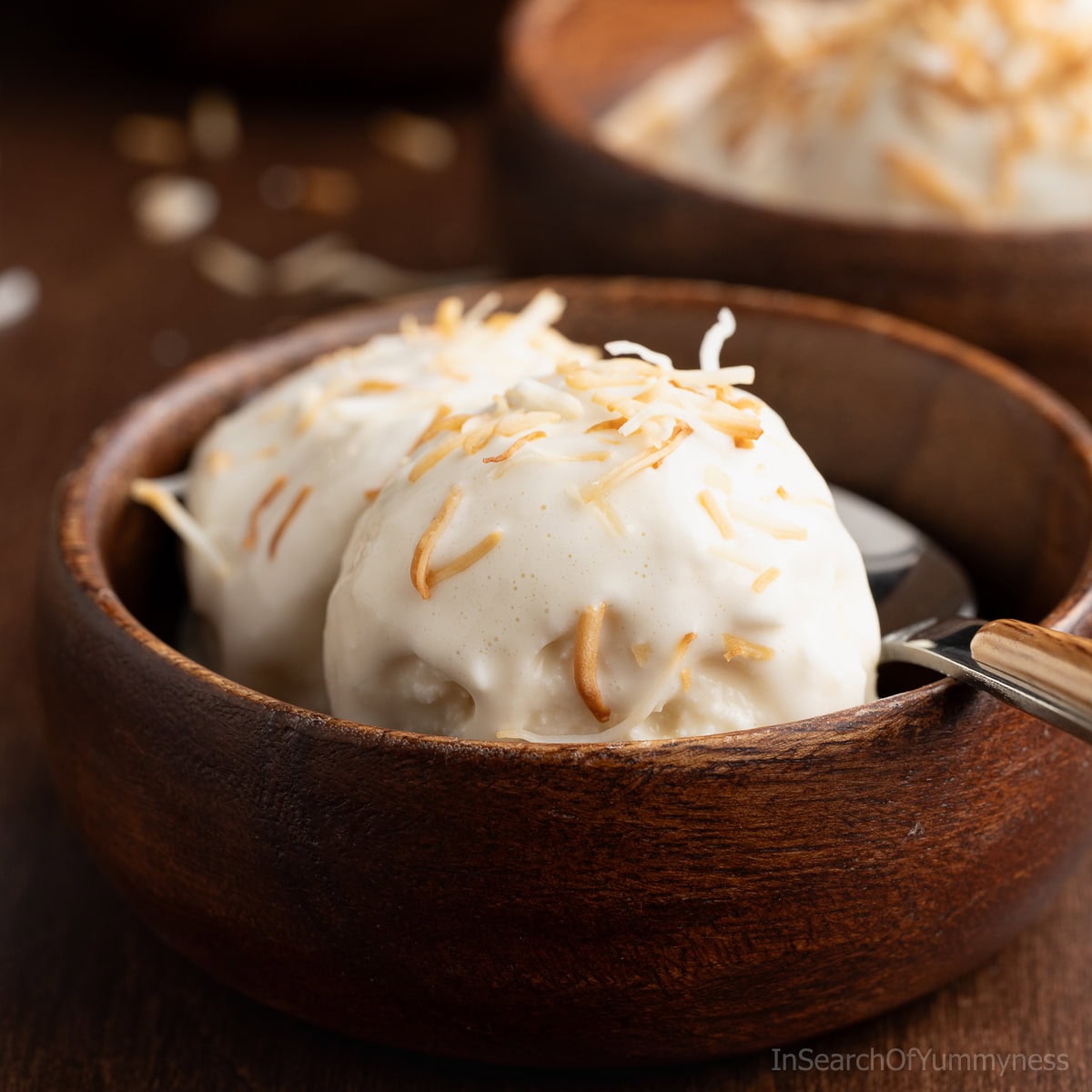 A wooden bowl with two scoops of Trinidad coconut ice cream, topped with toasted coconut.