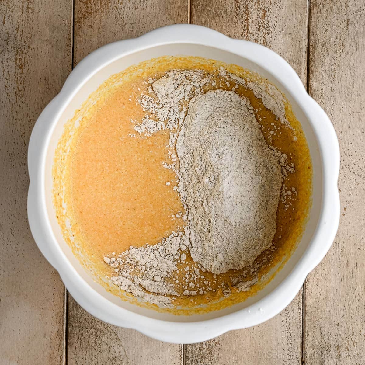 Adding the dry waffle ingredients to the wet waffle ingredients in a white pumpkin-shaped mixing bowl.