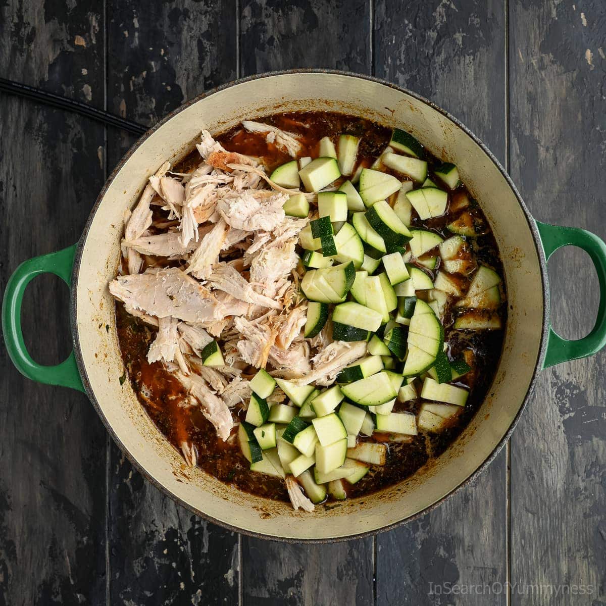 Shredded turkey meat and fresh diced zucchini being added to a pot of ingredients to make white turkey chili.