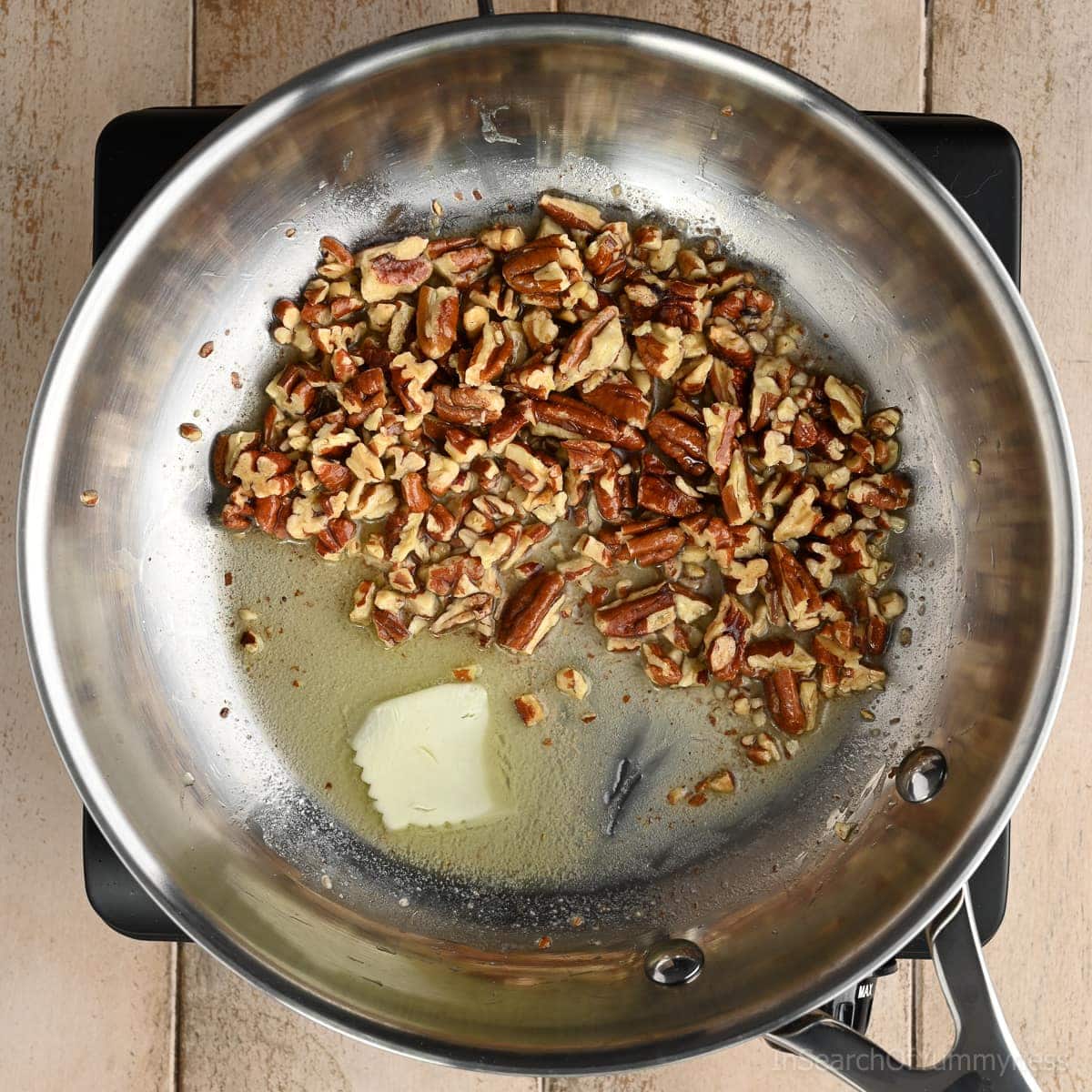 Toasted pecans in a stainless steel skillet with a melting pat of butter.