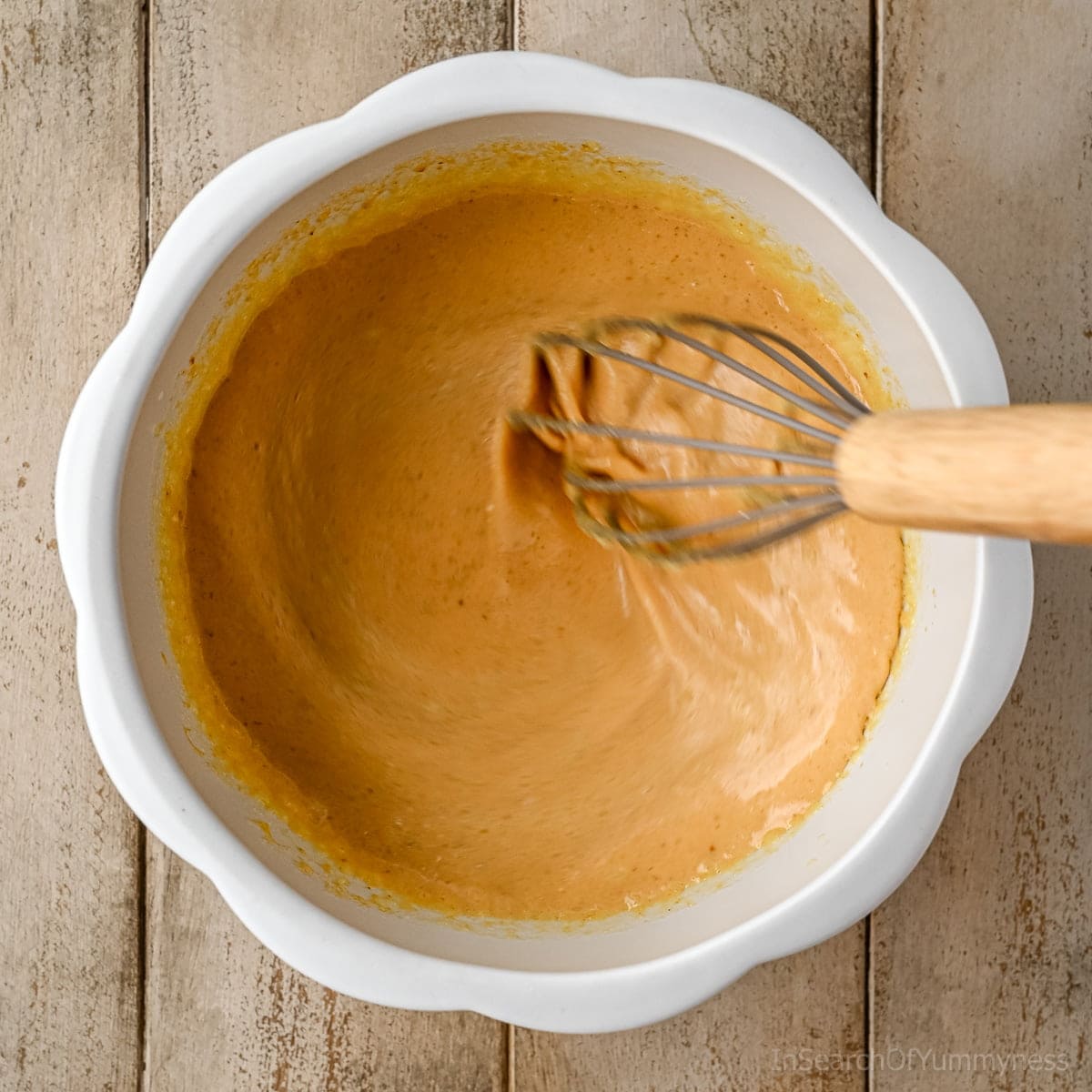 Whisking together the wet ingredients to make pecan pumpkin waffle batter in a white pumpkin-shaped mixing bowl.