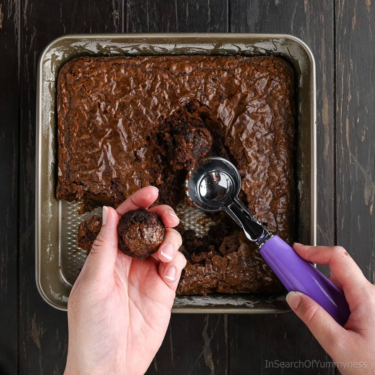 Hands using a cookie scoop to scoop out warm cooked browni to make round brownie balls.