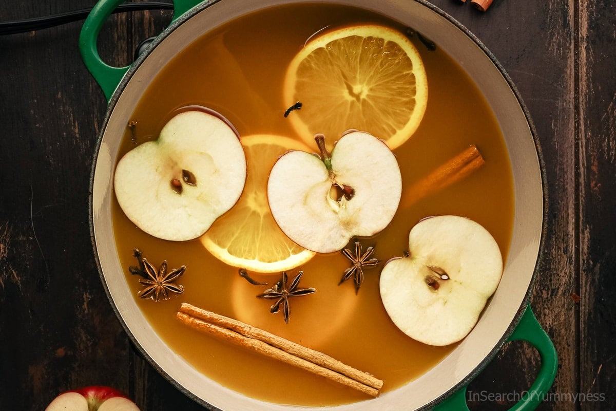 A green Le Creuset Dutch oven filled with warm spiced apple cider.