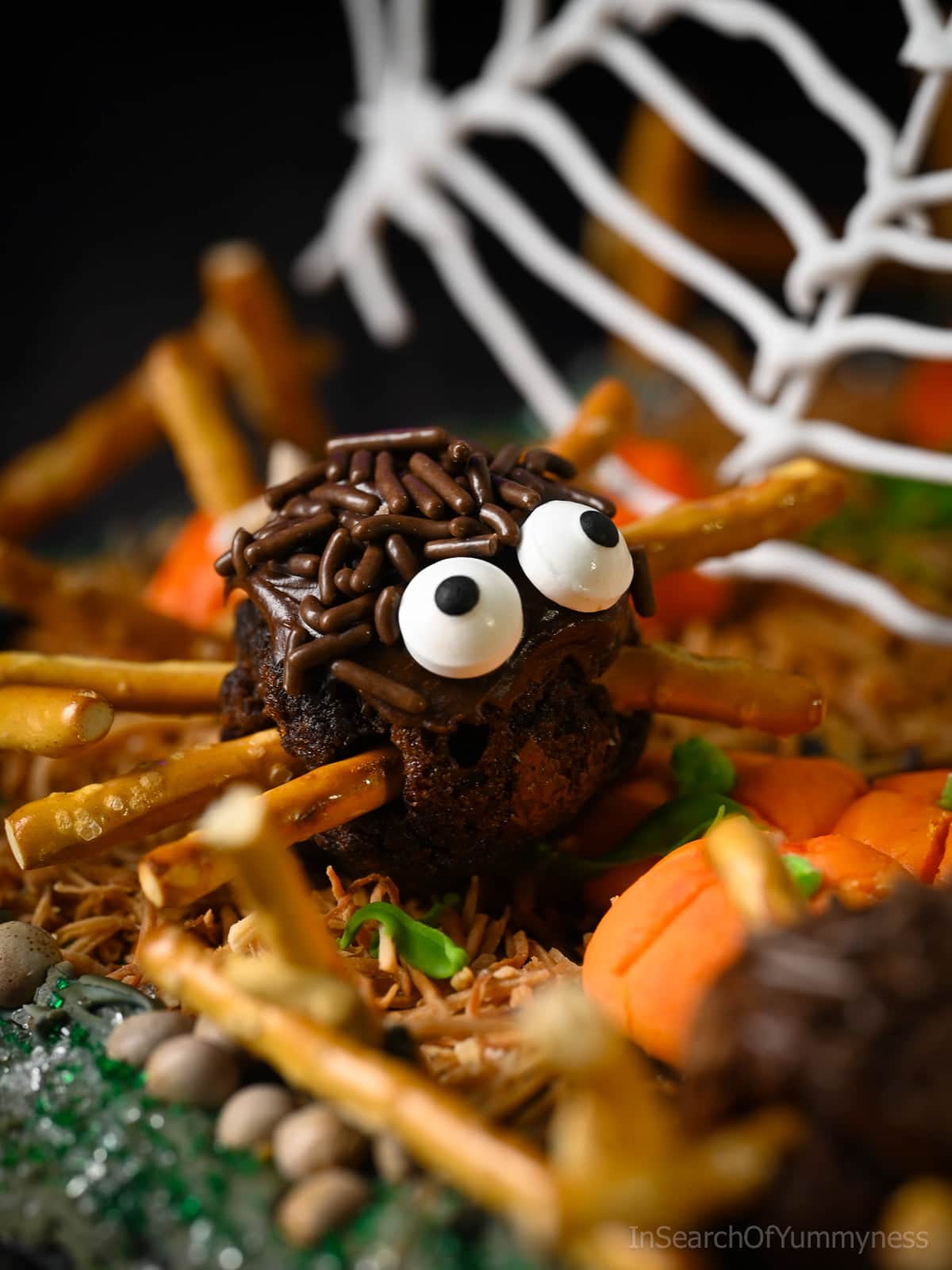 A decorated spider brownie sitting in a toasted coconut pumpkin patch with icing pumpkins.