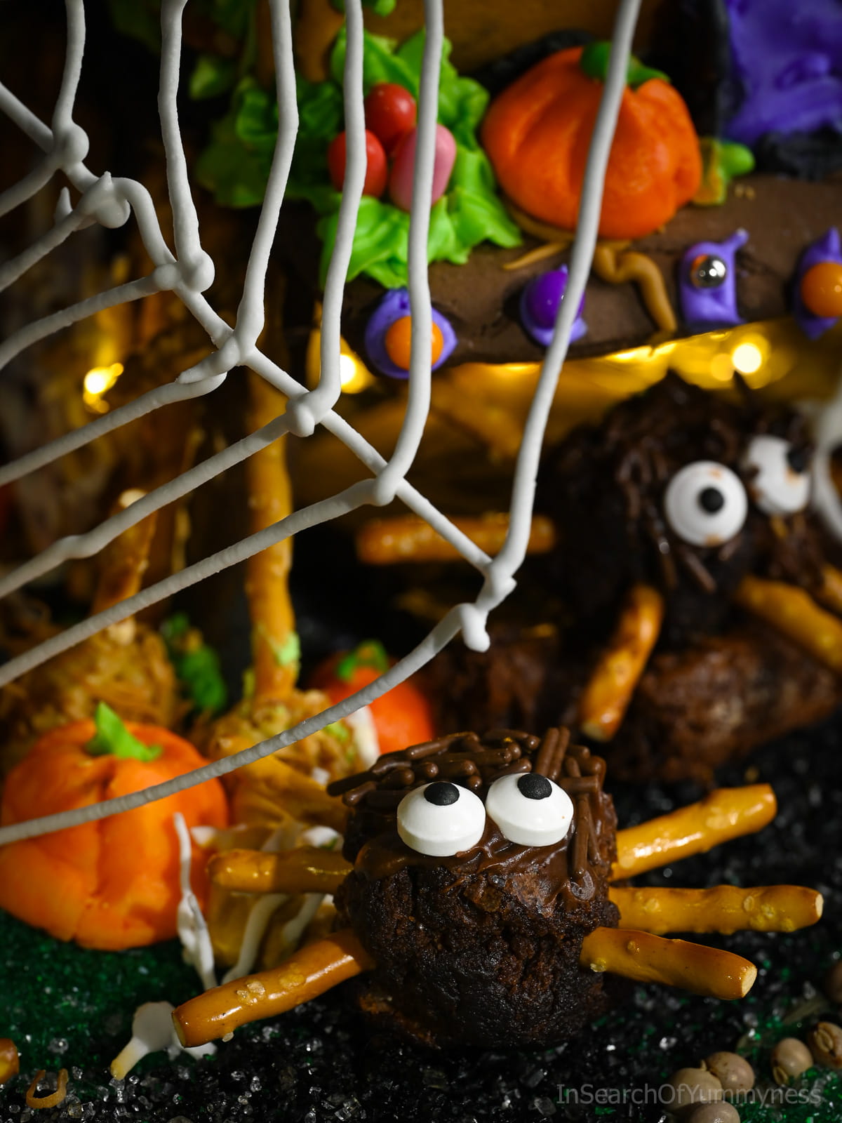 A decorated spider brownie sits under a giant white spider web, next to a pumpkin, with another spider brownie behind it.