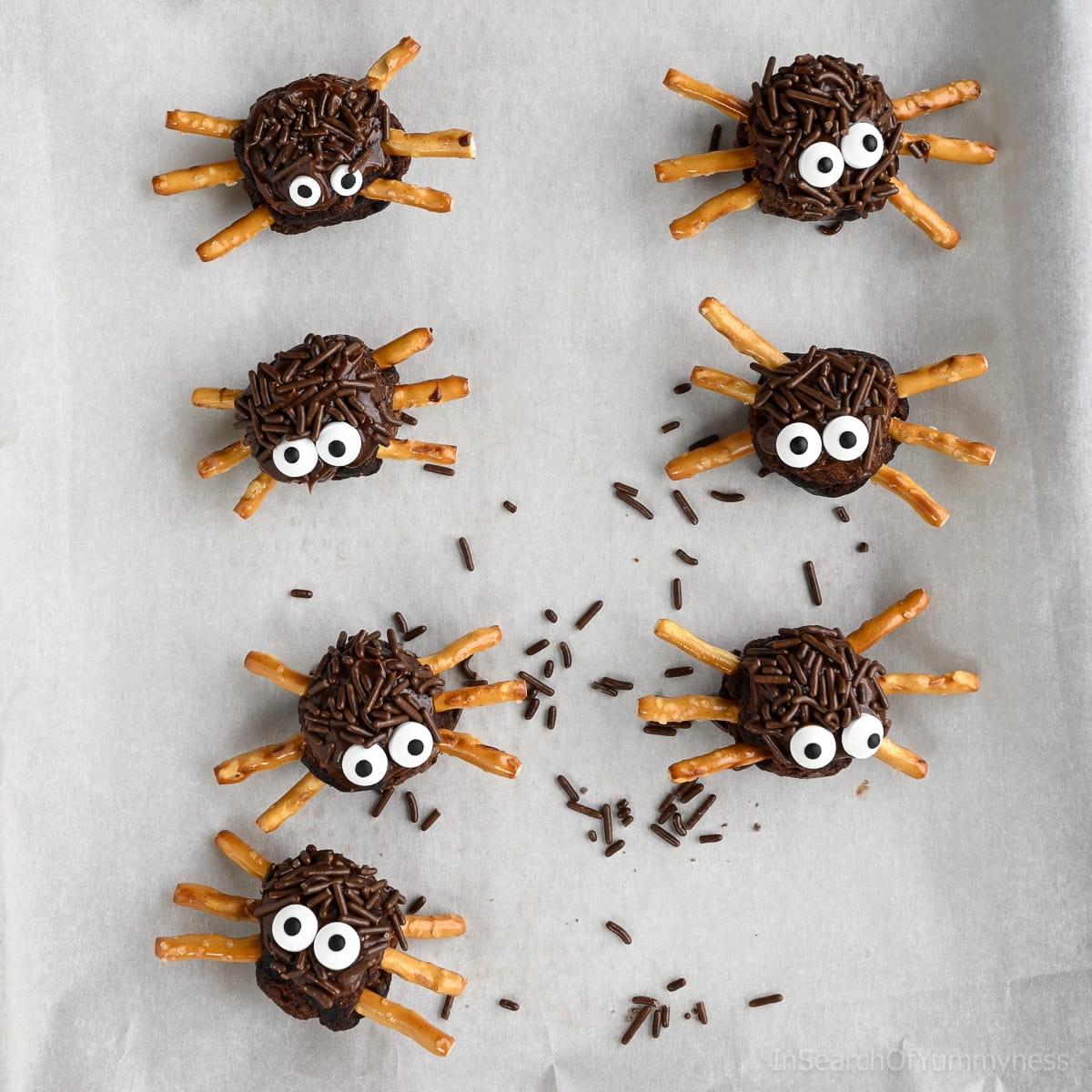 Seven finished spider brownies with pretzel legs on parchment paper.