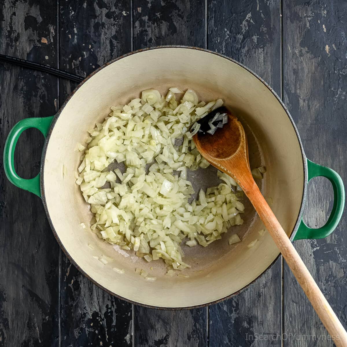 A green Le Creuset Dutch oven with a wooden spoon in it, and onions being cooked down.