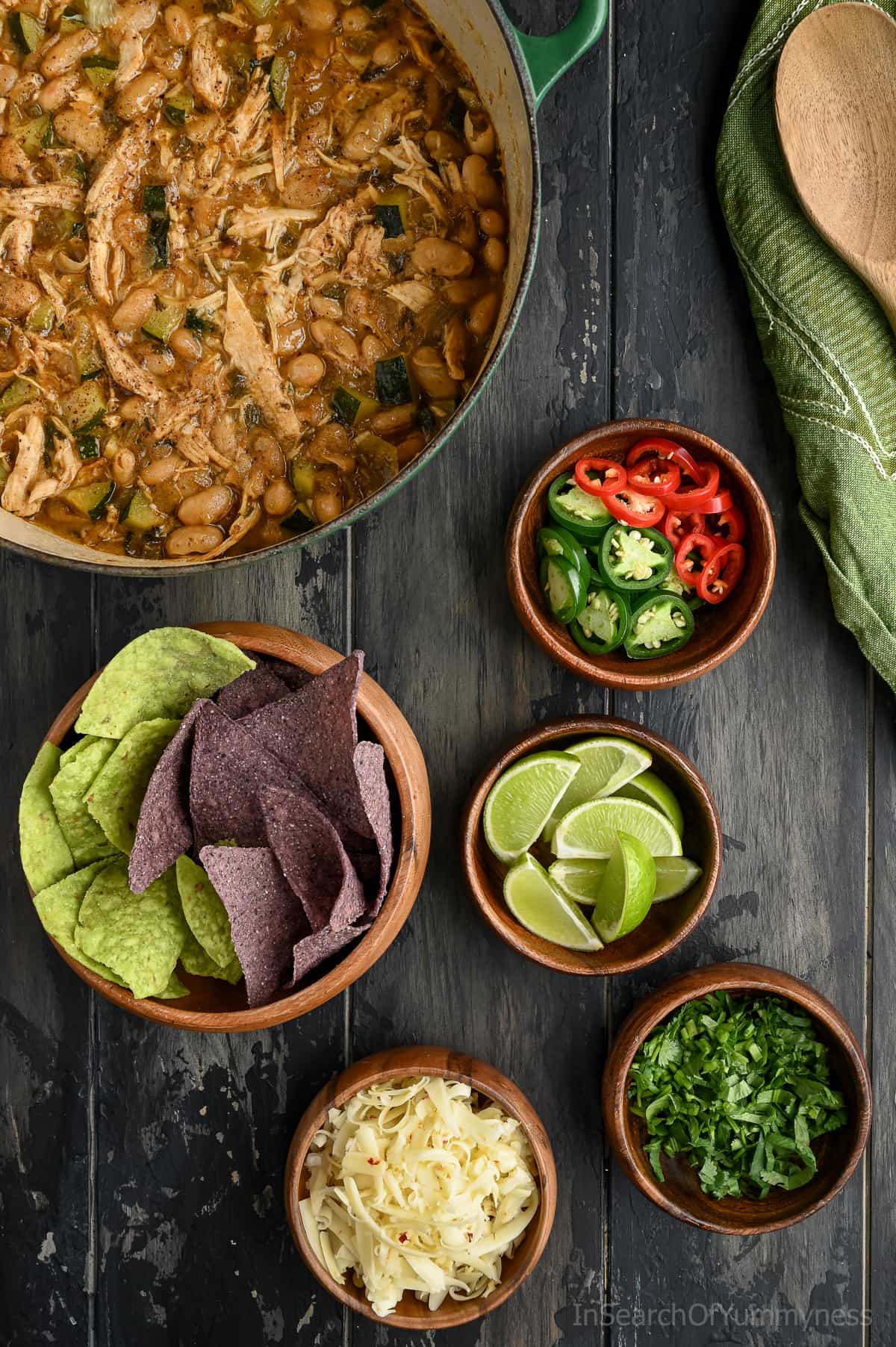 Overhead photo of white turkey chili in a pot with small bowls of toppings beside it, including tortilla chips, lime wedges, sliced jalapeños, chopped cilantro, and shredded cheese.