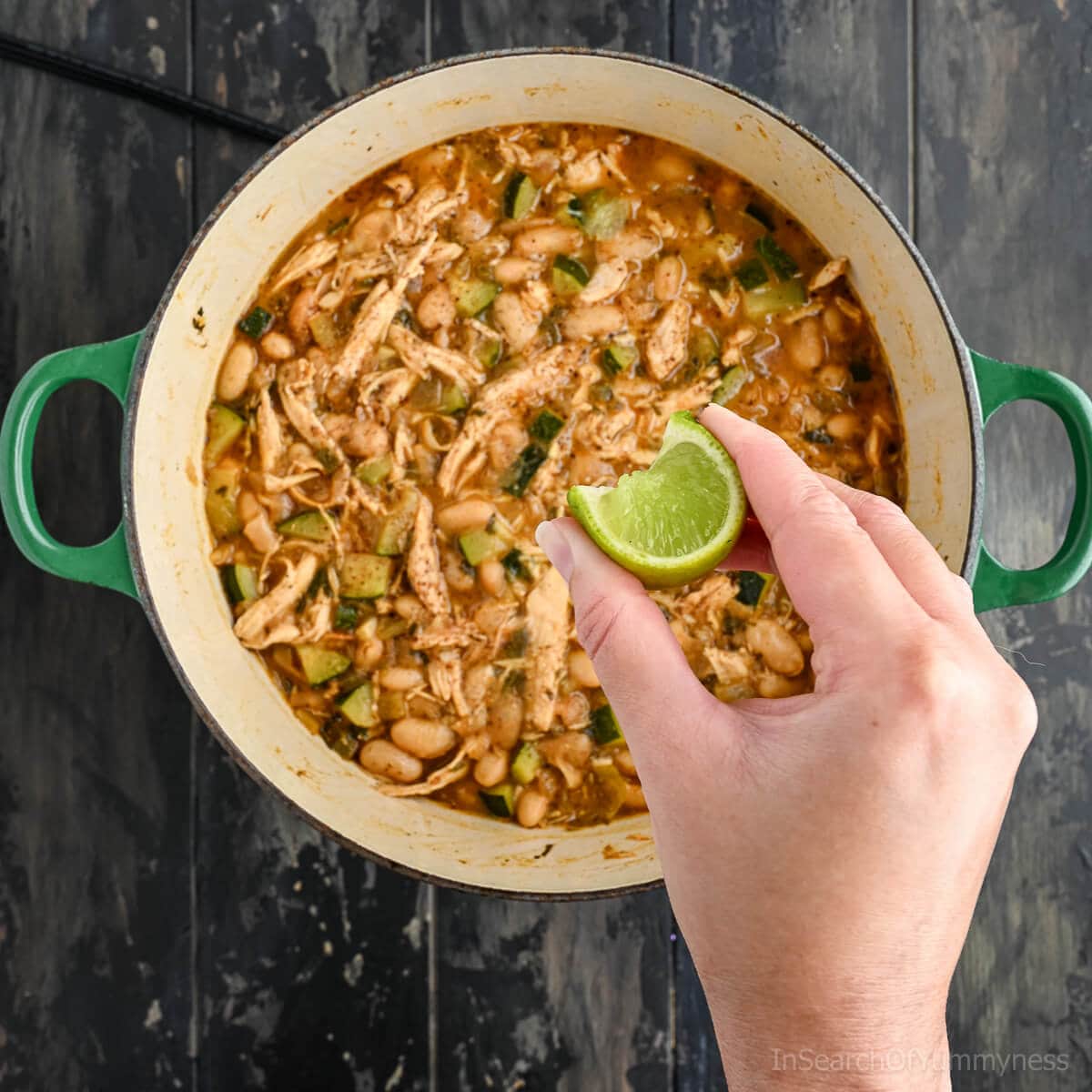 A hand squeezing a lime wedge over a pot of freshly cooked white turkey chili.