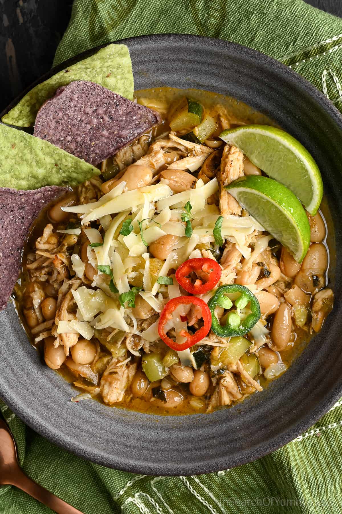 White turkey chili in a dark grey bowl, topped with sliced jalapeños, chopped cilantro, and shredded cheese. Served with tortilla chips and lime wedges.