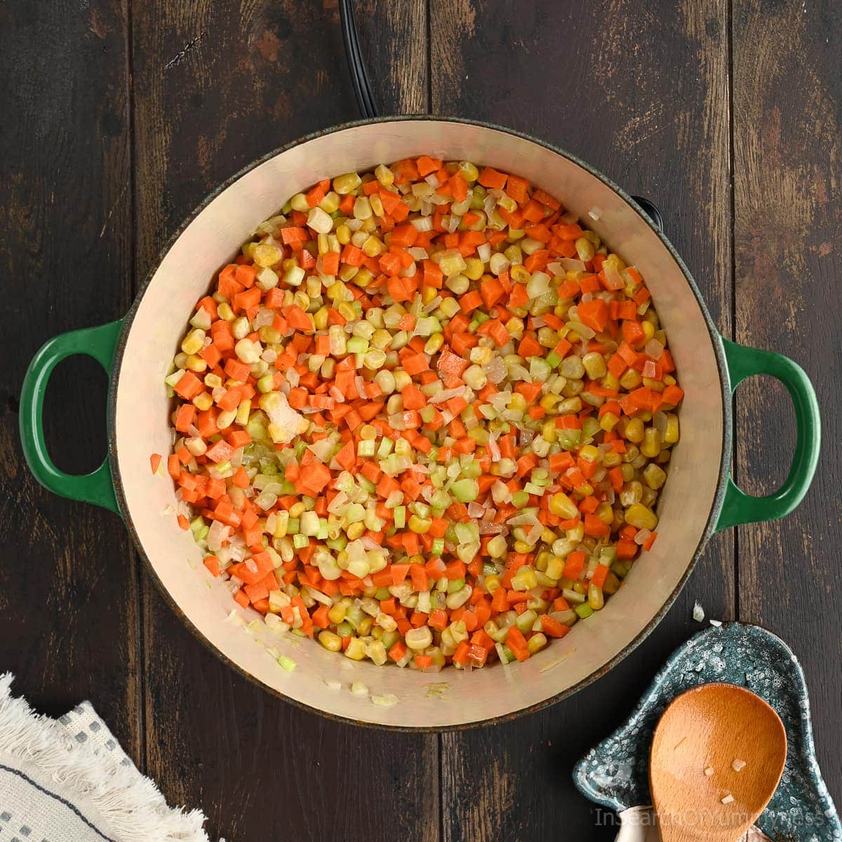 A Le Creuset Dutch oven with carrots, corn and celery sautéing in butter. The pot is on a portable electric burner.