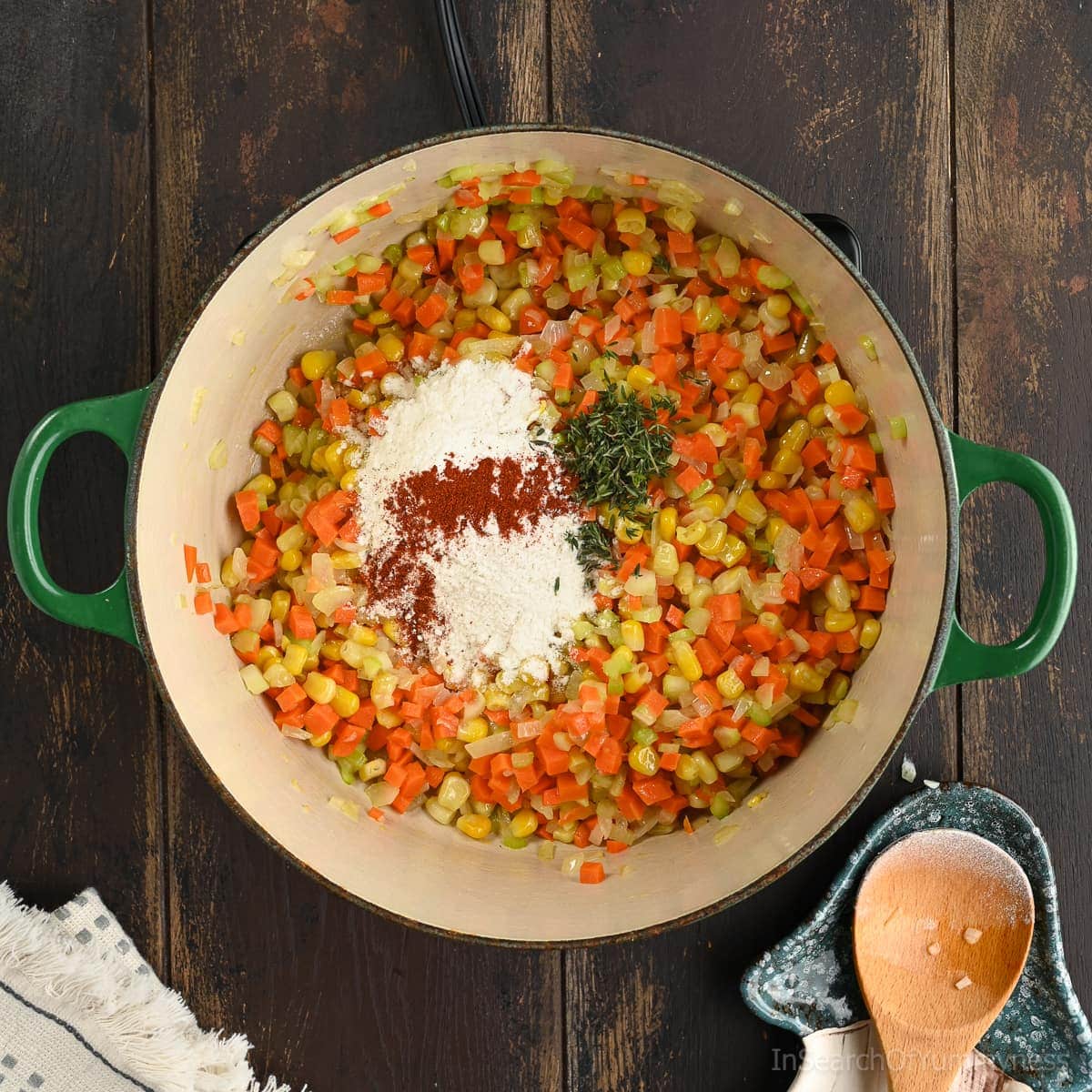 A Le Creuset Dutch oven with carrots, corn and celery sautéing in butter. Flour, paprika and thyme have been added to the pot now. The pot is on a portable electric burner.