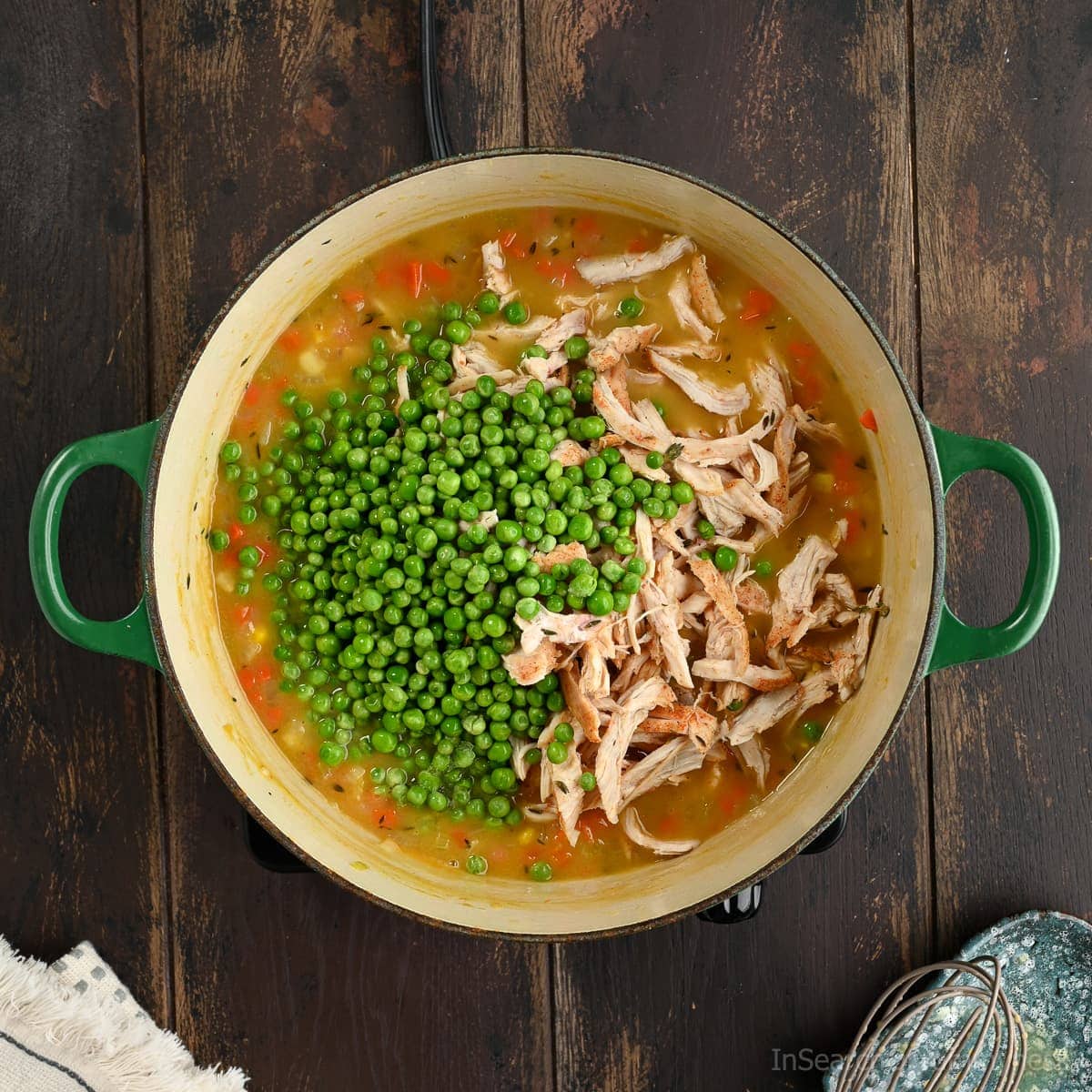 Adding frozen peas and shredded cooked chicken to the pot of soup.