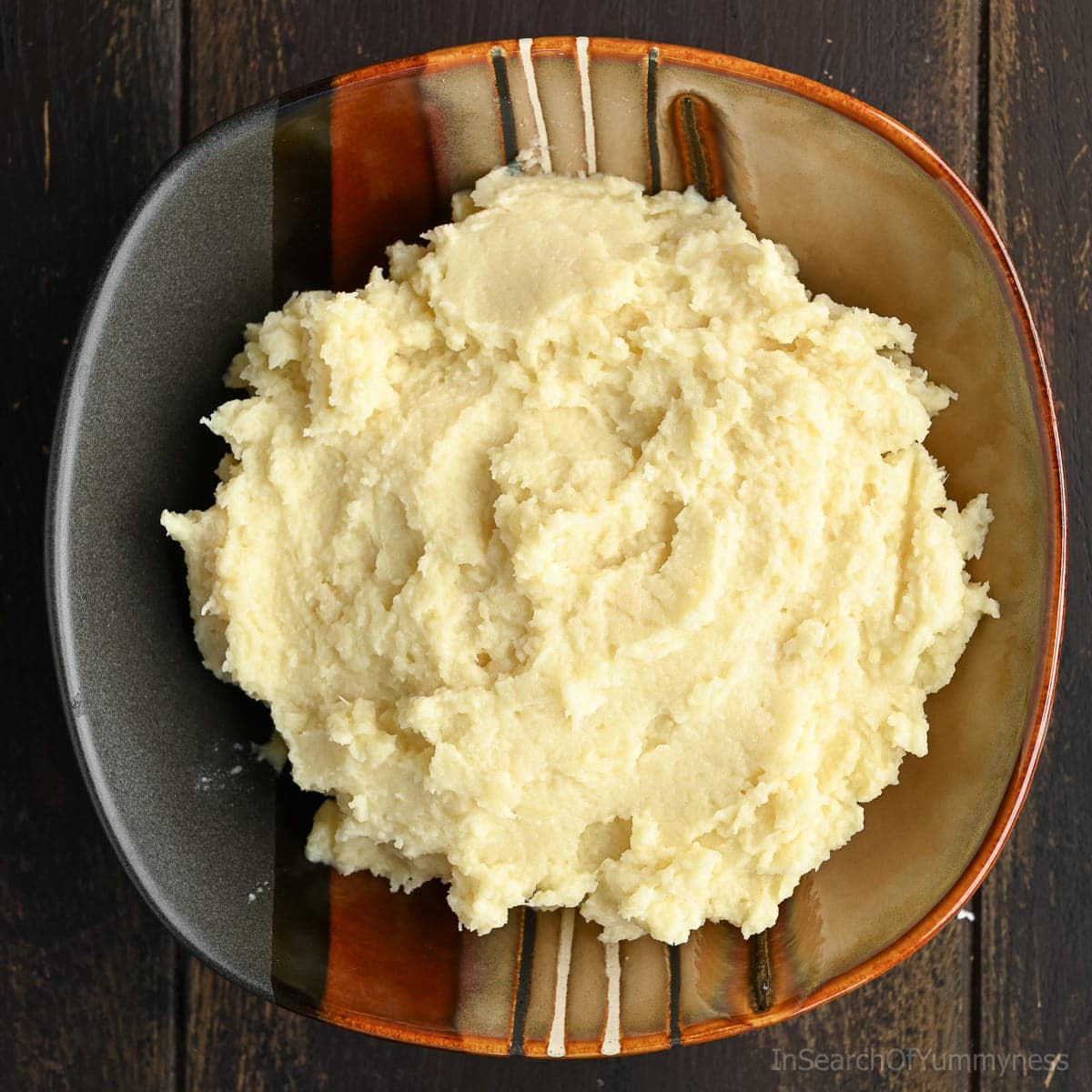 Mashed parsnips in a ceramic bowl, set on a dark wooden table.