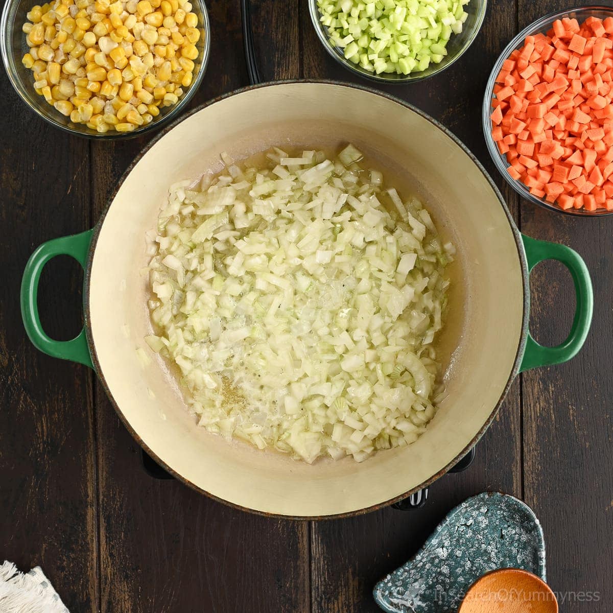 Diced onions softening in butter in a Dutch oven. There are bowls of vegetables around the pot as well.