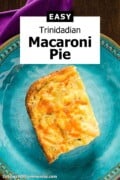 A slice macaroni pie with golden baked edges, specks of thyme, and bright orange flecks of cheddar cheese on top. Served on a blue plate next to a purple napkin. Text overlay says "Easy Trinidadian Macaroni Pie".