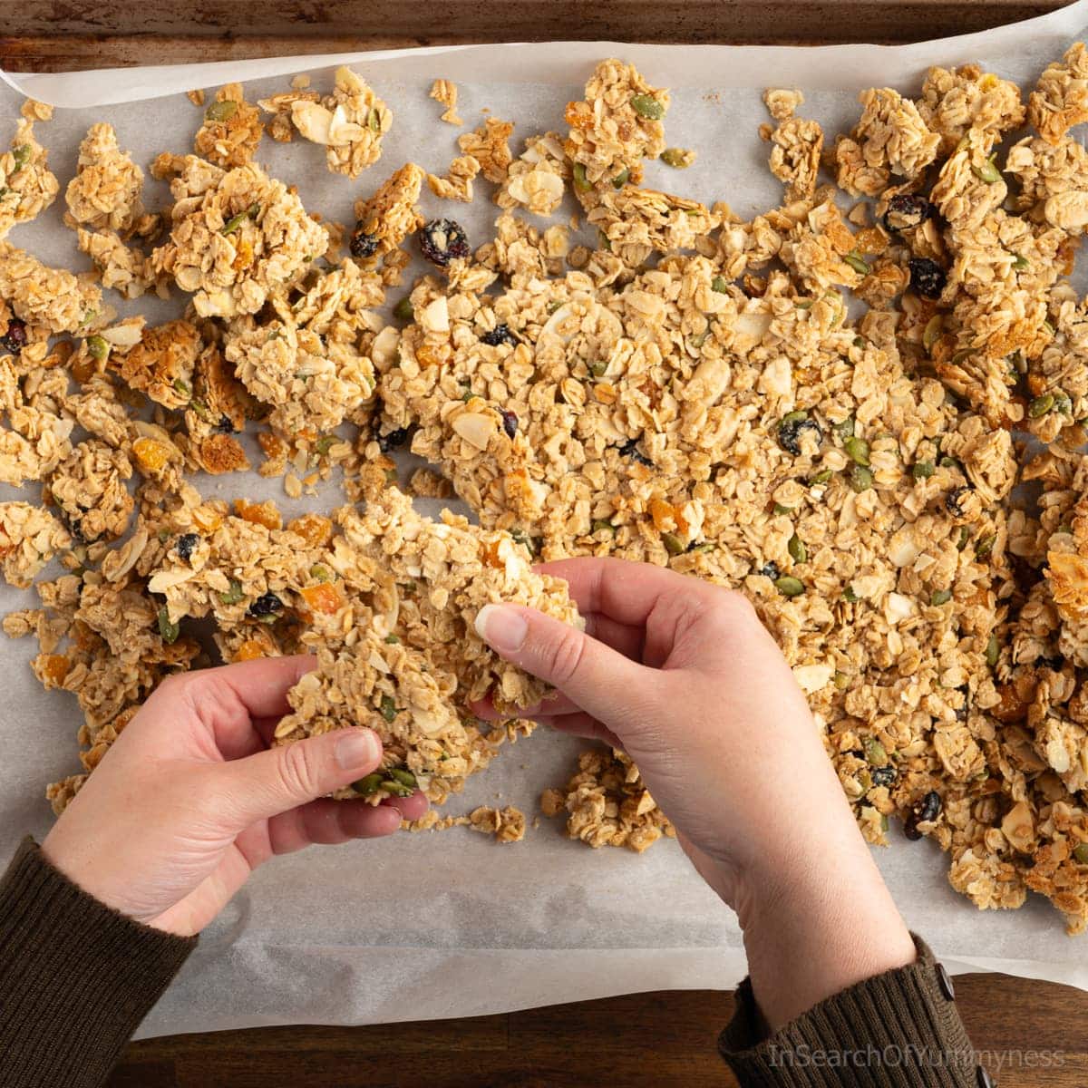 A pair of hands breaking freshly baked granola into clusters.
