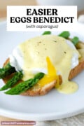 A runny poached egg on top of spears of cooked asparagus on a piece of toast, topped with Hollandaise sauce. Text overlay says "Easier Eggs Benedict with asparagus."
