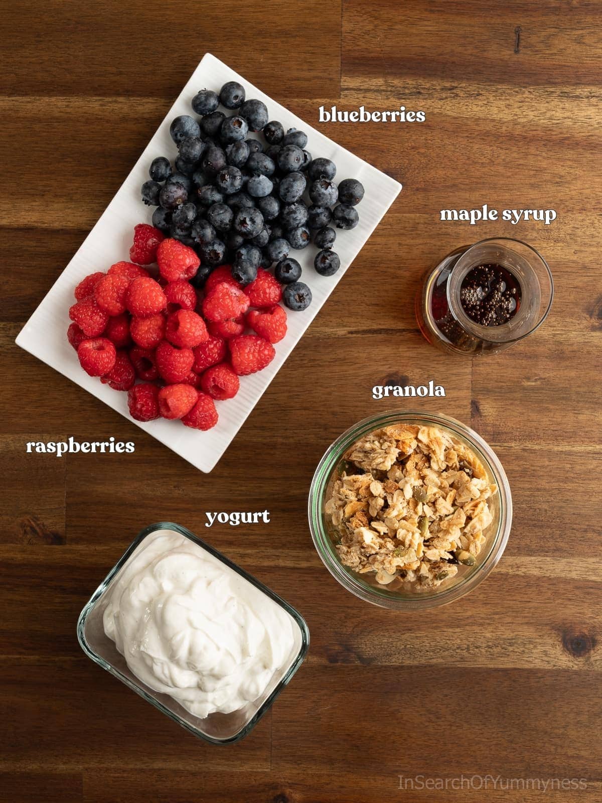 Ingredients needed to make a granola parfait including yogurt, berries, granola and maple syrup.