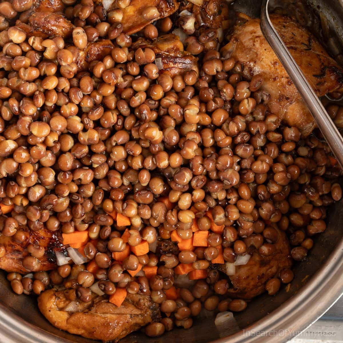 Dry pigeon peas in a stainless steel pot, with chicken, onions and carrots to make Trinidadian pelau.