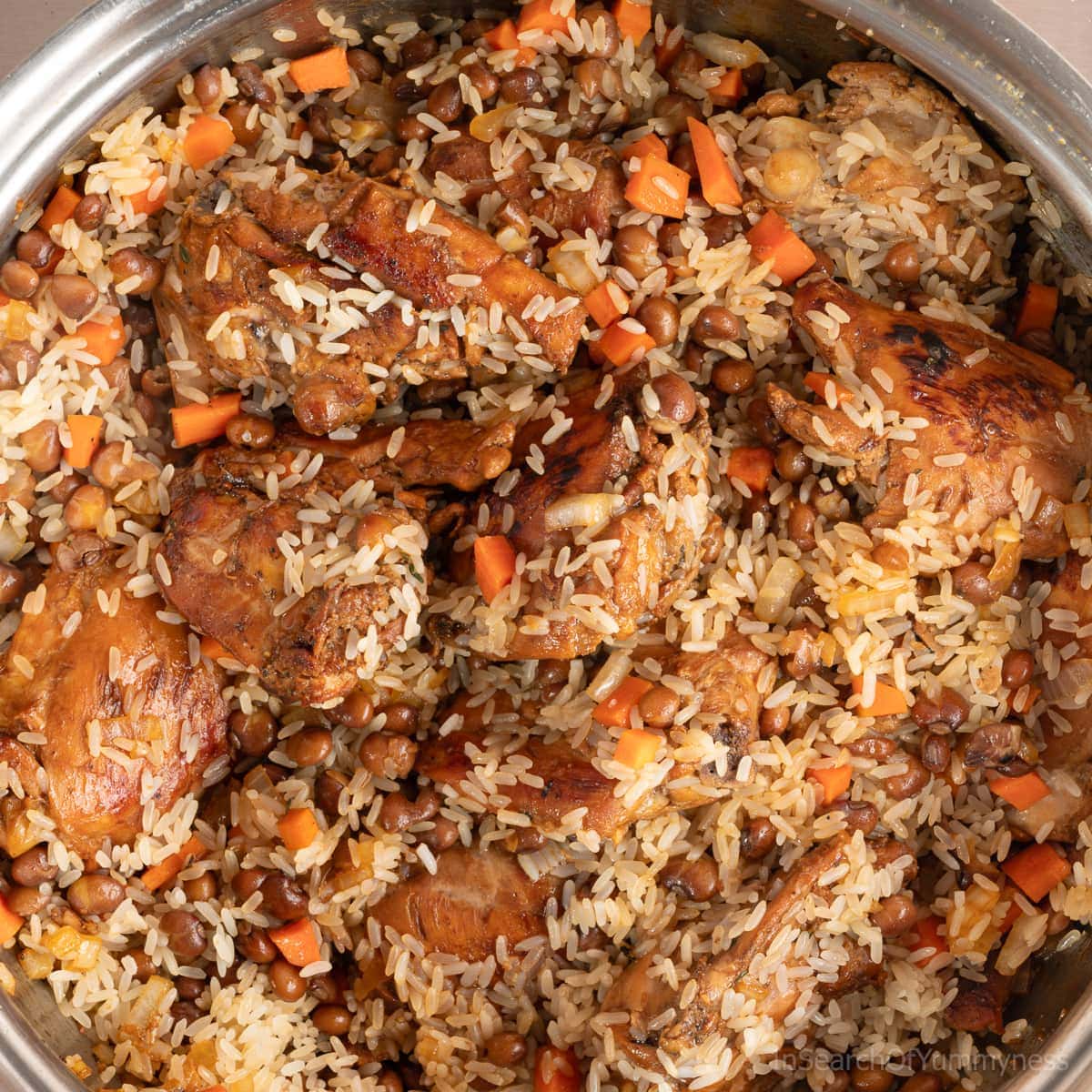 A stainless steel pot full of browned chicken, rice, carrots and onions.