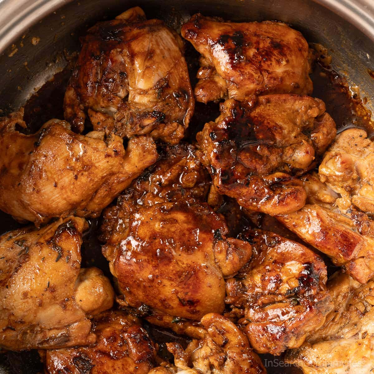 Chicken browning in caramelized brown sugar and oil in a stainless steel pot for Trinidadian pelau.