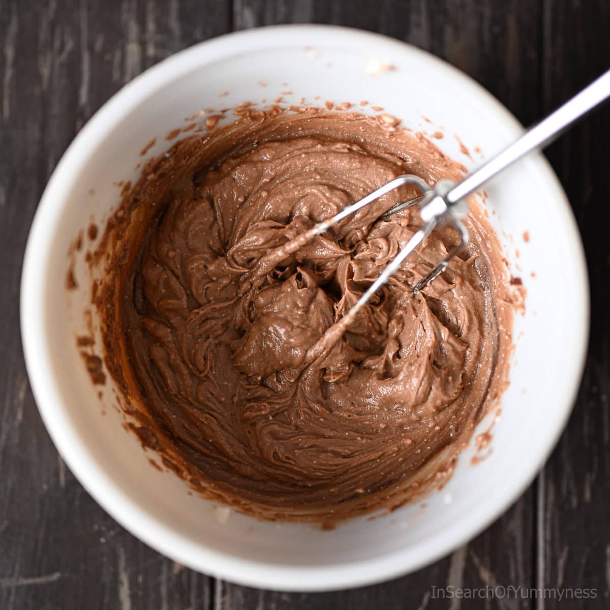 A white mixing bowl with a hand mixer beater laying on top of mixed mascarpone cream.