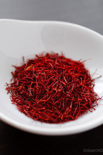 Strands of saffron in a white bowl on a brown wooden table.